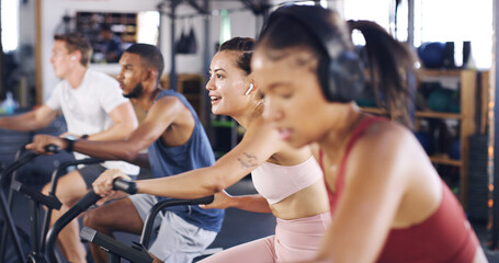 Fototapeta premium Spin class, fitness and earphones with woman in gym for intense workout, music and cycling challenge. Cardio, streaming and stationary bike machine with people in sports club for health and energy