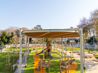 Aerial view of a vibrant playground with green turf and orange pathways under a pergola, surrounded by trees, Bat Yam, Center District, Israel.