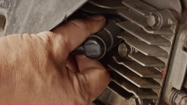 Close-up hand removing black spark plug cap from motorcycle engine fins