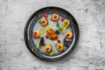 Top view of an elegant gourmet appetizer plate with assorted canapés topped with pâté and berry sauce, caramelized fruit, fresh raspberries, grapes, microgreens, and artistic fine dining presentation