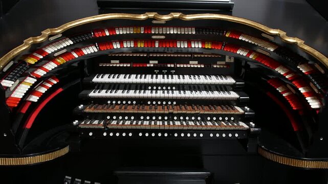 An organ labeled Wurlitzer is displaying multiple keyboards stop tabs and curved rows of controls framed in gold trim within a black wooden structure