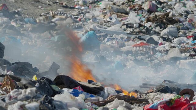 Fire and smoke rise from pile of burning garbage in landfill, pollution, waste management issues, and environmental damage. Close-up