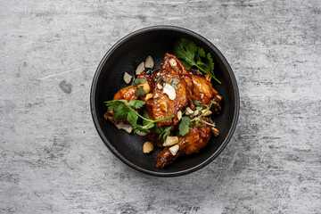 Glazed chicken wings with cashew nuts and fresh cilantro served in a black ceramic bowl on gray rustic background