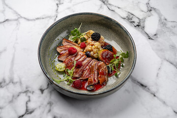 Gourmet duck breast fillet with berry sauce, fresh raspberries, blackberries, figs, grapes, cauliflower and microgreens served on ceramic plate with marble background