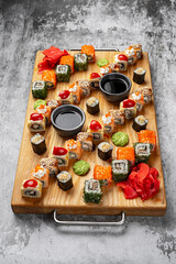 Assorted sushi rolls with salmon, nori, sesame, cream cheese, tobiko, pickled ginger and wasabi served with soy sauce on a wooden board for Japanese cuisine presentation