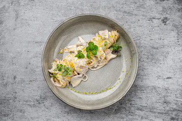 Spaghetti pasta with creamy white sauce, grated cheese, fresh herbs and ham served in ceramic bowl on gray stone background, close up