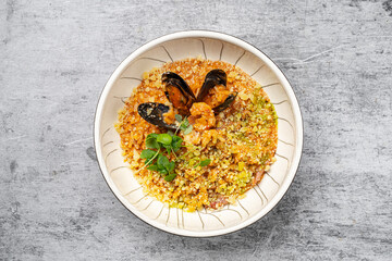 Seafood risotto with mussels, shrimp, parmesan cheese and fresh herbs served in a ceramic bowl on gray stone background, traditional Italian cuisine