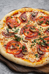 Italian pizza with salami, fresh tomato slices, mushrooms and parsley on melted cheese baked on a wooden board over rustic background