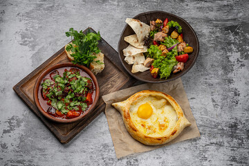 Georgian cuisine assortment with khachapuri, meat stew with herbs, fresh salad with pita bread and vegetables on rustic gray background