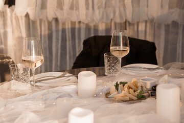 Romantic Dinner Setting: Two Wine Glasses, Cheese Plate, Soft Lighting, White Drapery, Intimate Ambiance, Warm Tones, Elegant Table Decor, Cozy Mood.