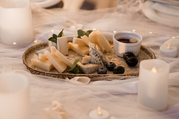 Romantic Indoor Picnic with Cheese Board, Candles, and String Lights: Cozy Night, Soft Focus, Warm Tones, White Linen, Intimate Setting.