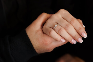 Romantic Engagement: Hands Holding Diamond Ring, Couple, Love, Proposal, White Gold, Close-up, Black Background, Intimate Moment, Celebration.