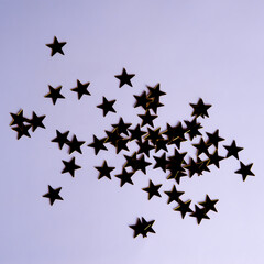 Star-shaped sequins silhouettes on purple background, top view, copy space for festive design.