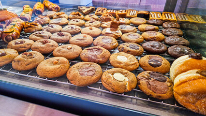 A variety of cookies displayed in a bakery. The assortment includes chocolate chip, oatmeal, and peanut butter cookies on a cooling rack.