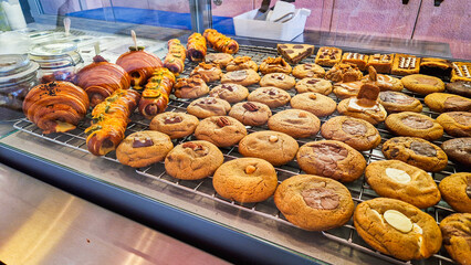 A variety of cookies displayed in a bakery. The assortment includes chocolate chip, oatmeal, and peanut butter cookies on a cooling rack.