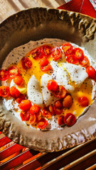 A plate of scrambled eggs topped with sliced cherry tomatoes. The dish is garnished with black pepper and served on a textured ceramic plate.