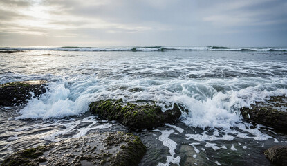 Ocean waves crashing over rocky shoreline during cloudy evening  