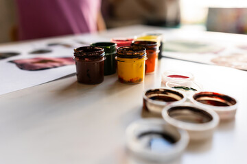 Variety of colorful paint jars on artist's workspace with artwork in background
