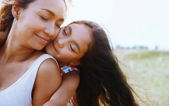Mother and daughter embracing outdoors in nature with loving smiles