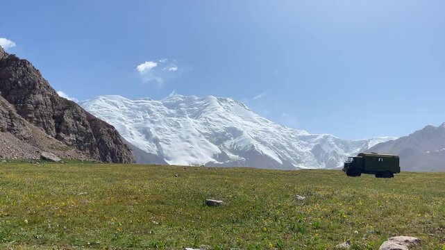 Incredible wide angle panoramic 4K video shot of Pamir mountains range near from Lenin peak base camp at cca 3800m with slowly moving milytary colors truck driving mountain road on Onion meadows field