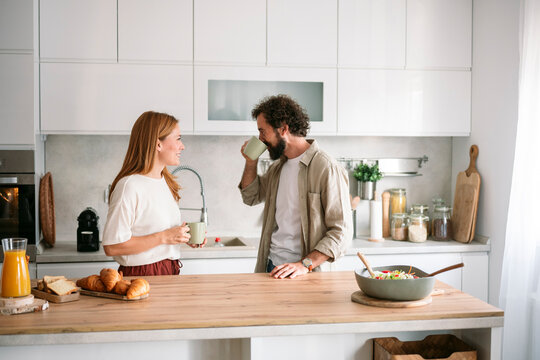 Happy couple talking and having breakfast in modern kitchen
