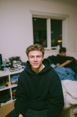 Young man in casual hoodie playing video games at home on bed with relaxed expression
