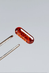 Translucent amber capsule held by tweezers on neutral background, macro pharmaceutical supplement and clinical research detail