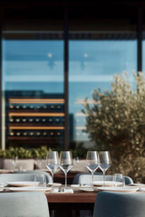 Elegant restaurant table by large window with city view, two glasses of red wine and fine dining place settings in modern urban bistro interior at golden hour