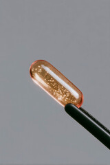 Translucent amber capsule held by tweezers on neutral background, macro pharmaceutical supplement and clinical research detail
