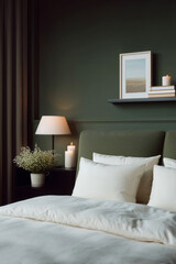 Cozy modern bedroom with deep green accent wall, soft white bedding, bedside lamp and candles, Scandinavian minimal interior design with hygge atmosphere