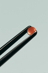 Minimal macro of small round tablet gripped by black tweezers on soft green background, precision dosage and pharmaceutical quality control