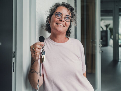Smiling woman with glasses leaning by the entrance holding keys