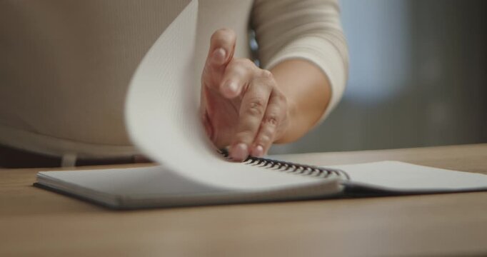 Close up of a woman hands tearing out blank pages from a spiral bound notebook on a wooden table. Slow motion.