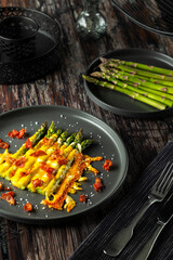 Asparagus spears baking with melted cheese and bacon crumbs