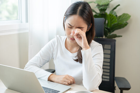 Tired asian young woman burnout, stressed from problem work at desk in office, looking at laptop computer, feeling sick, pain eye strain rubbing dry irritated eyes fatigued working late on deadline. - Powered by Adobe