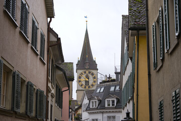 Citycape with alley and church tower with clock face of Saint Peter church at the old town of Swiss city of Zürich on cloudy and rainy autumn day. Photo taken October 27th, 2025, Zurich, Switzerland.