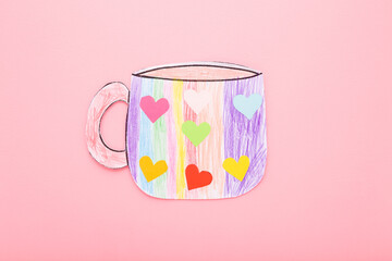 Paper mug shape painted with colorful pencils and glued with hearts. Kid handcraft on light pink table background. Pastel color. Closeup. Top down view.