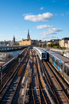Blue metro train crossing elevated railway bridge over Stockholm city skyline near Gamla Stan, representing urban transport infrastructure and sustainable travel through Scandinavian design context