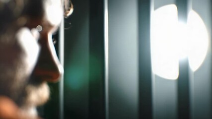 Close-up profile of a bearded man gazing out a window, sunlight streaming through vertical blinds. - Powered by Adobe