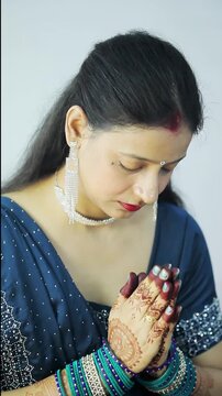 Indian woman in blue saree offering puja with namaste gesture for festival celebration