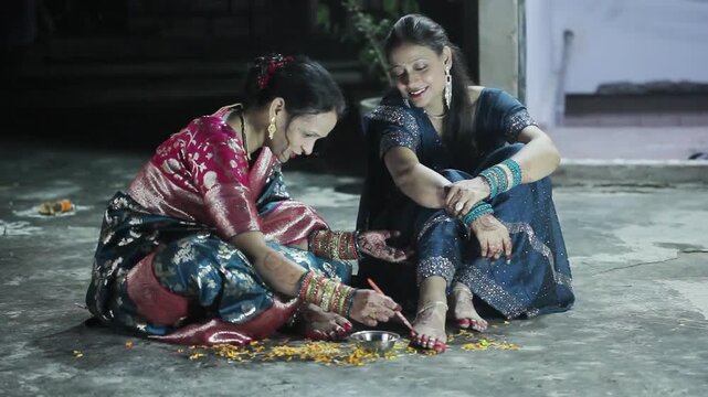Two Indian women applying aalta (a traditional red dye) on their feet before Hindu puja and festival celebration