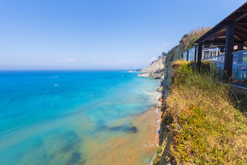 Modern cliffside restaurant overlooking a pristine turquoise ocean with clear shallow water and sandy shore
