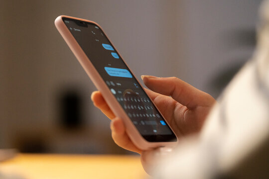 Crop anonymous female using smartphone and messaging on app at home against blurred background