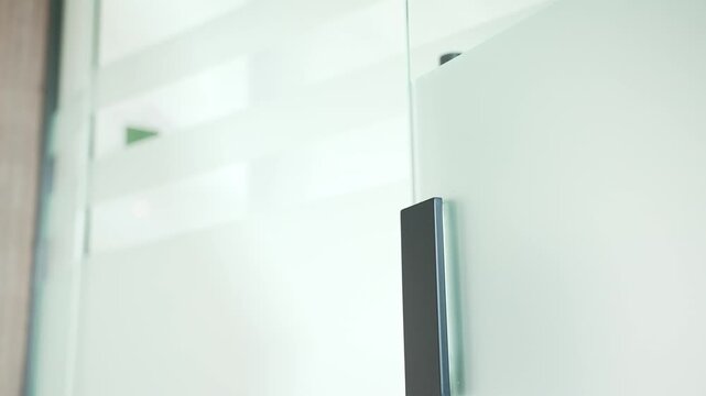 Close up of african american businesswoman opening a glass office door pushing a metal doorknob with hand. Female employee in jacket opens the door and enters the office to workplace. Rear side view