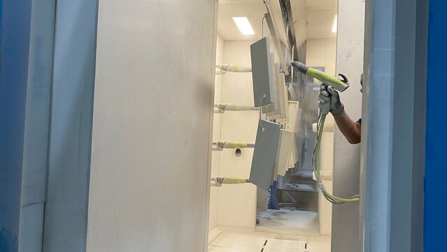 Industrial worker using an electrostatic spray gun for powder coating metal parts in a manufacturing factory.