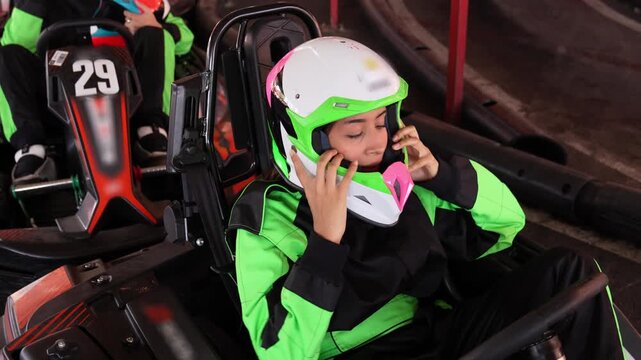 Female racer sitting in a go kart putting on her safety helmet and grabbing the steering wheel, ready for the race on an indoor circuit