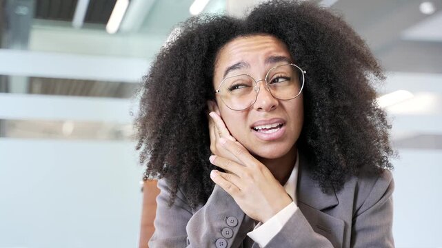 Unwell african american businesswoman suffers from ear pain sitting in office. Woman touches her ear with her fingers. She has furuncle, shingles, eczema, ear diseases, otitis media. Earache. Close up