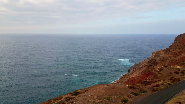 Fototapeta Drone deep blue ocean water crashing dangerous rocky shoreline creating foam.