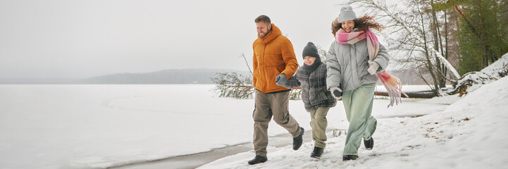 Header of Caucasian man, woman, and child walking together along snowy lakeshore, holding hands and...