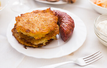 Potato pancakes with fried sausage on white plate